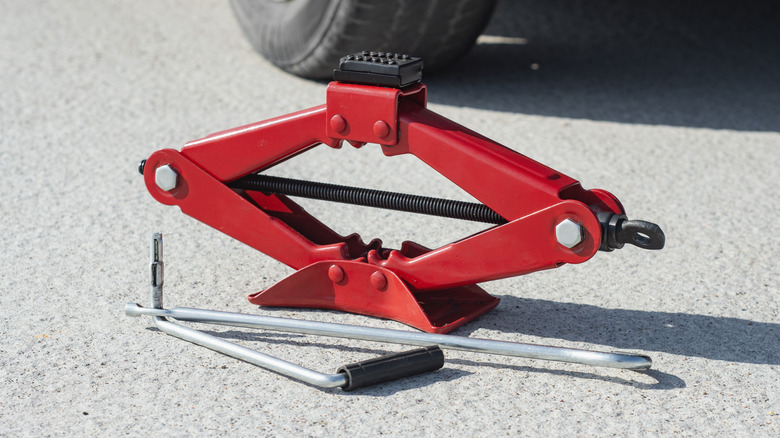 A red automotive scissor jack sitting upright near a car