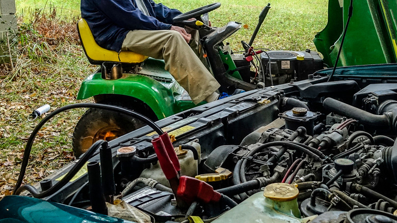 A man on a lawn mower tries to jump start the lawn mower from the car battery