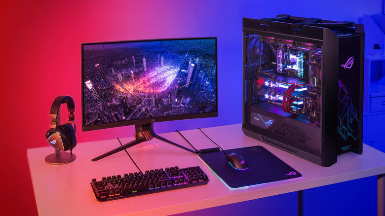 ASUS ROG Strix gaming desktop computer showing tower, monitor, headphones, mechanical keyboard, and mouse on desk, red-blue lighting