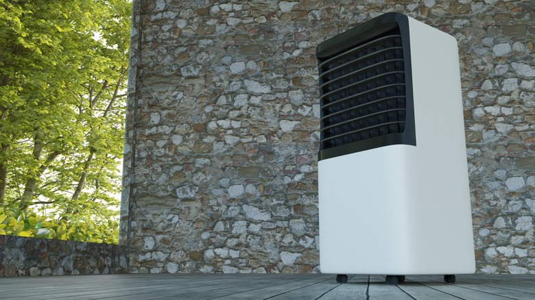 A portable air conditioner placed on a deck next to a stone wall.