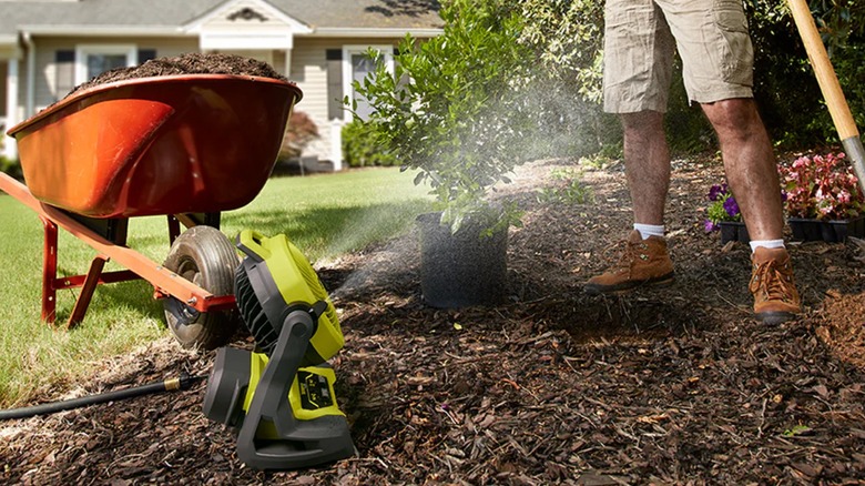 A Ryobi misting fan next to a person performing gardening work