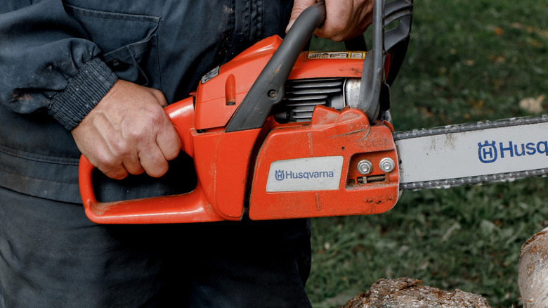 A person holding a Husqvarna chainsaw outside.