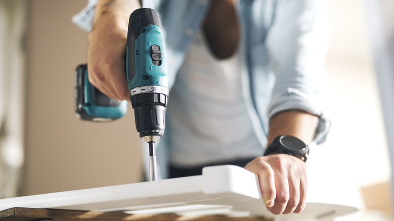 Close-up of person using electric screwdriver to assemble furniture.