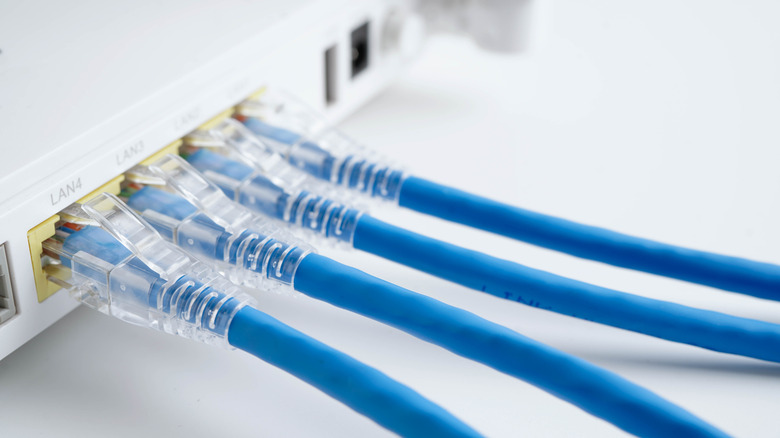 A white router placed on a table with four Ethernet cables connected to its LAN ports