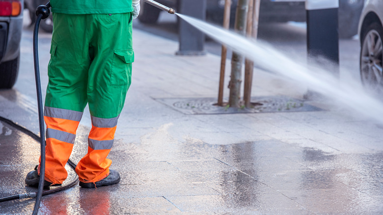 A worker cleaning a sidewalk with a pressure washer.