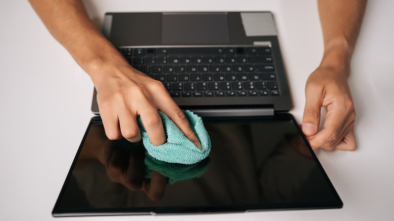 Person using a microfiber cloth to clean a laptop screen.