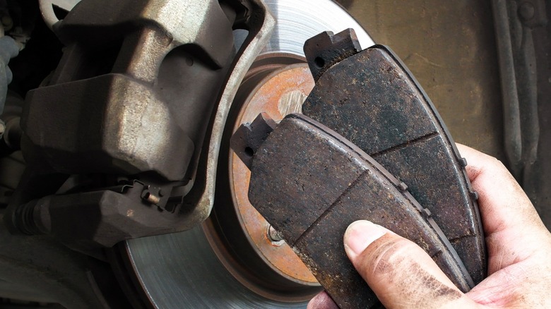 a person holding old brake pads in front of a disc brake assembly