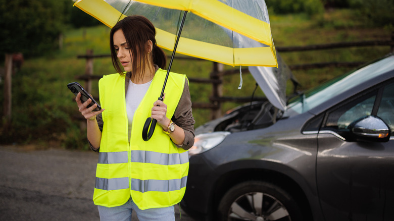Woman with umbrella, phone, car with open hood in background