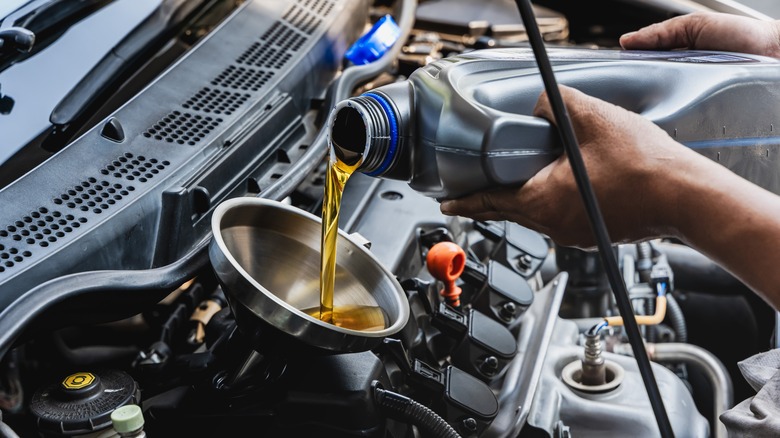 person pouring engine oil into vehicle through funnel