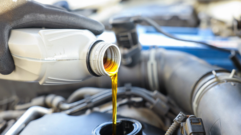 A gloved mechanic pouring new oil into a car's engine