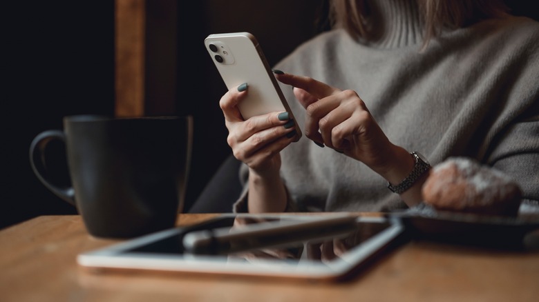 person holding iPhone with iPad on table