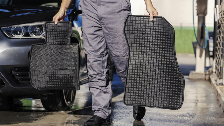 A person removing dirty mats from a car.