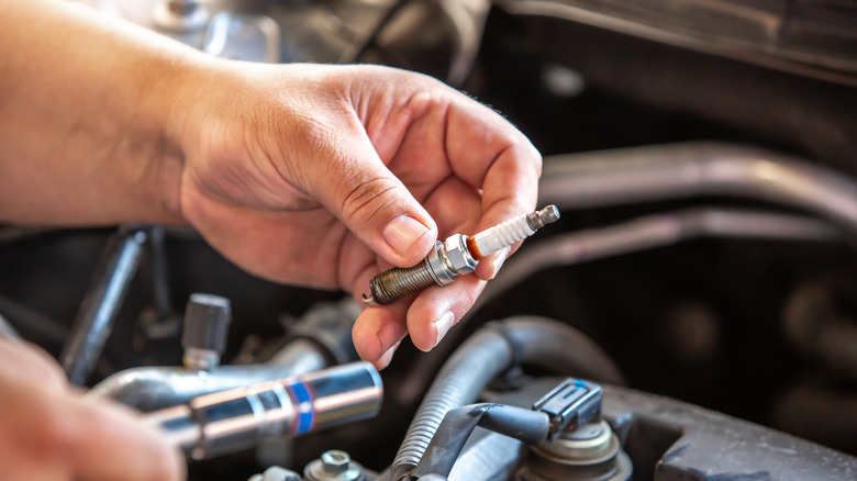 A close-up of a person holding a used spark plug over the engine.