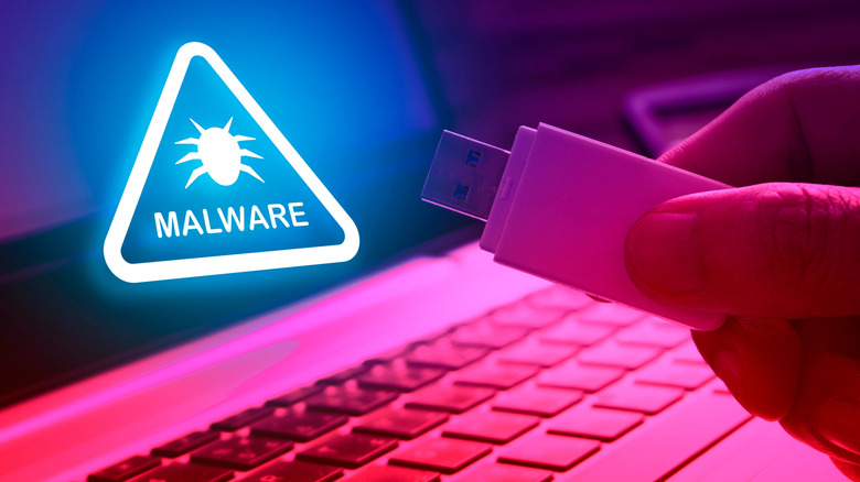 A hand holding a USB flash drive with malware icon over laptop