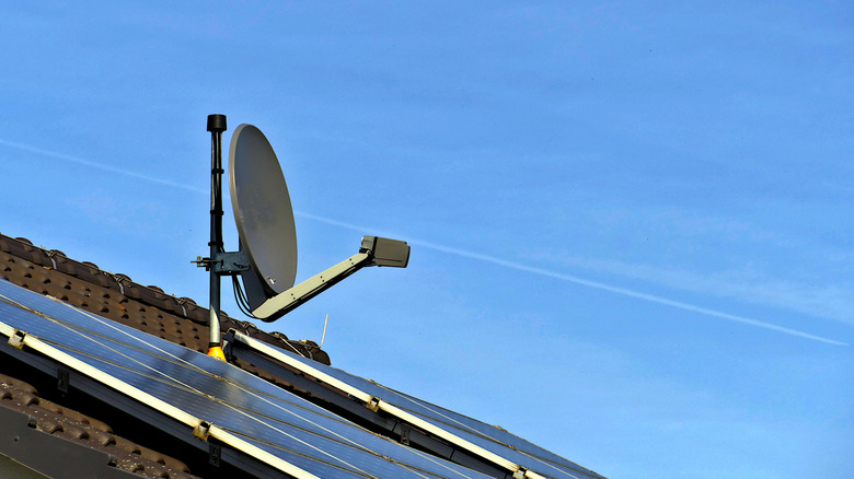 A satellite dish and solar panels on a roof against a blue sky
