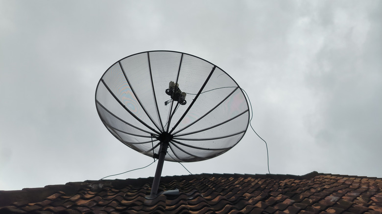 A satellite dish on roof tiles against a cloudy, overcast sky