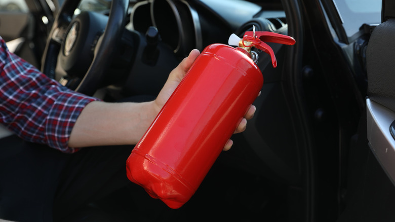 A man's hand holding a fire extinguisher in car