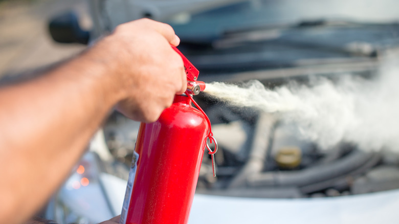 Someone using a fire extinguisher to put out a car fire