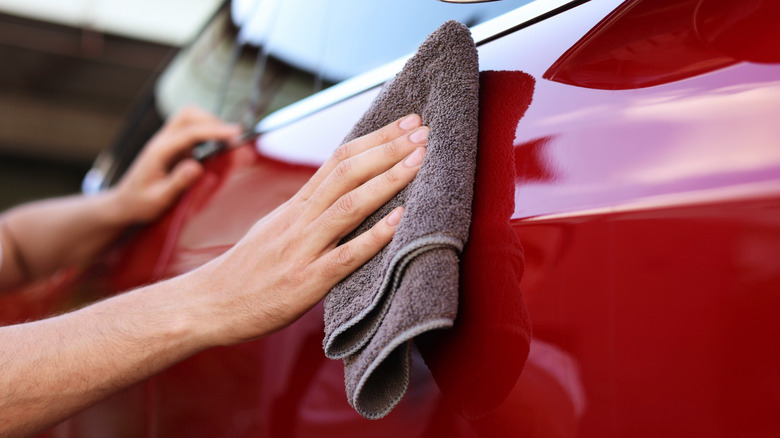 A person wiping a red car with a microfiber cloth.