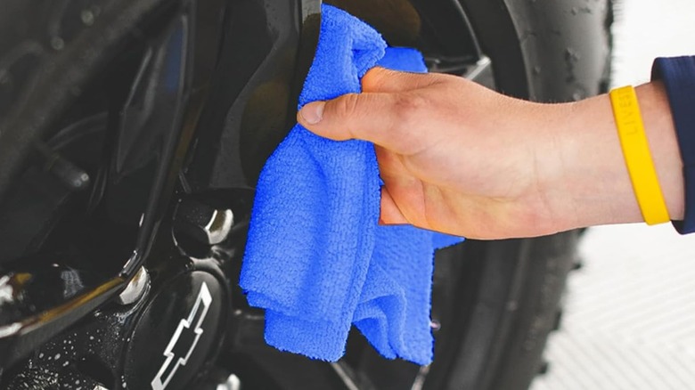 A person wiping a car rim with a microfiber cloth.