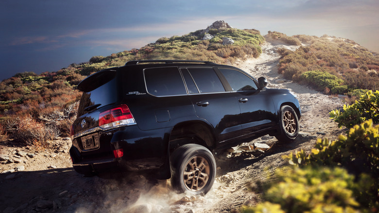 A dark colored Toyota Land Cruiser 200 Series heritage special edition off-roading, kicking up dust at speed.