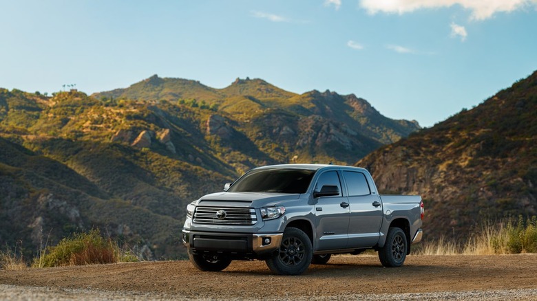 A silver-gray 2021 Toyota Tundra pickup truck parked off the beaten track on mud, with hills in the back.