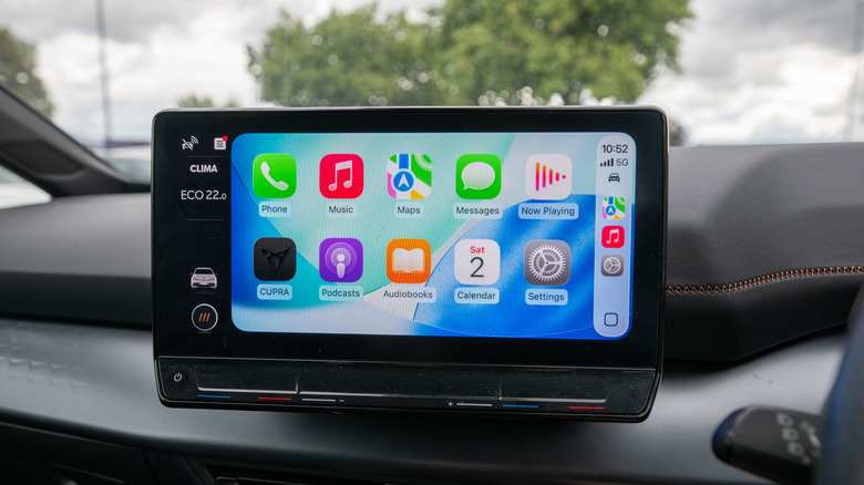 A close-up of a person interacting with Apple Car Play on a car's center screen.