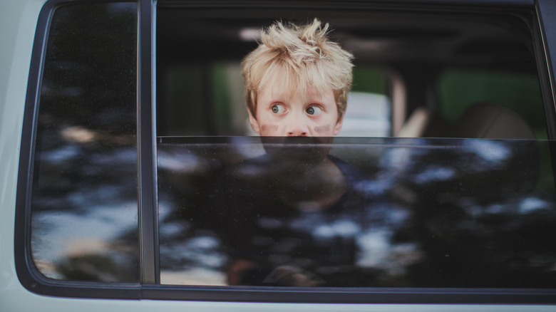 Blond-haired boy looking out half-open tinted rear car window