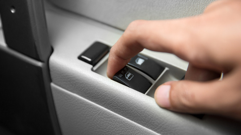 Close-up hand pressing button automatic power controlling window in car.