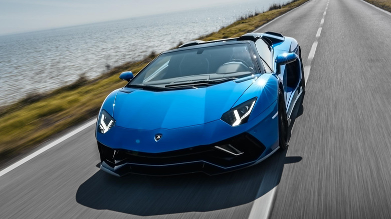 A blue Lamborghini Aventador driving down a road, seen from the front.