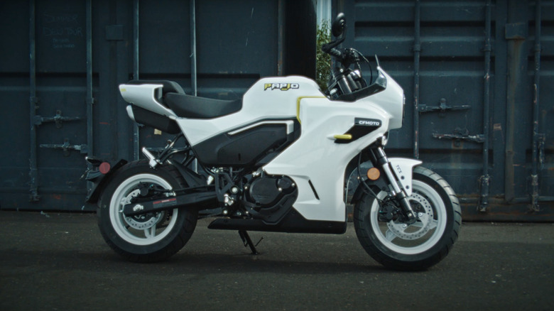 A white CFMoto Papio propped up, side view, shipping containers in the background
