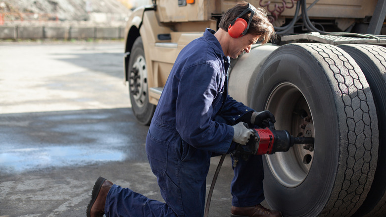 Mechanic wearing ear protection using air compressor drill to bolt a new tire to a a semi-truck