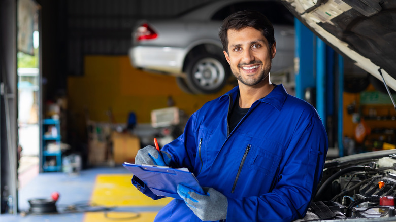 Mechanic with clip board leaning on car