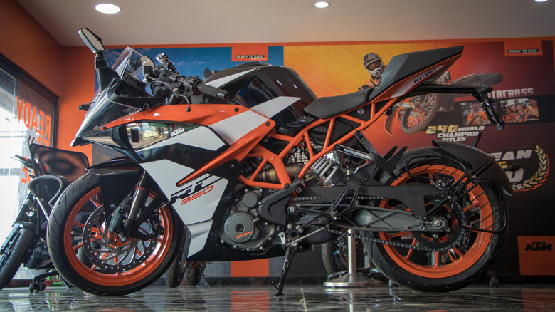 An orange and white KTM Duke RC 390 sport bike parked on its kickstand in an indoor location.