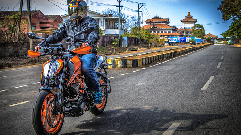 A rider in a full face helmet and leather jacket riding a KTM Duke 390 down the highway, front view.