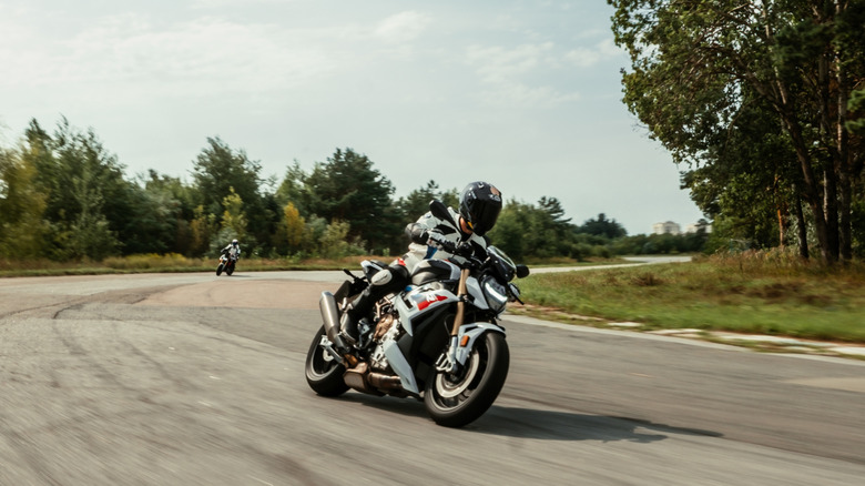 A white BMW S1000R taking a corner on a closed racetrack at speed, with the rider wearing full-body protection and a helmet.