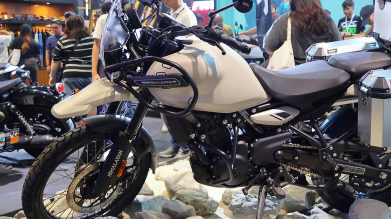 A Royal Enfield Himalayan 450, finished in white, on display to a crowded room at an indoor trade show.