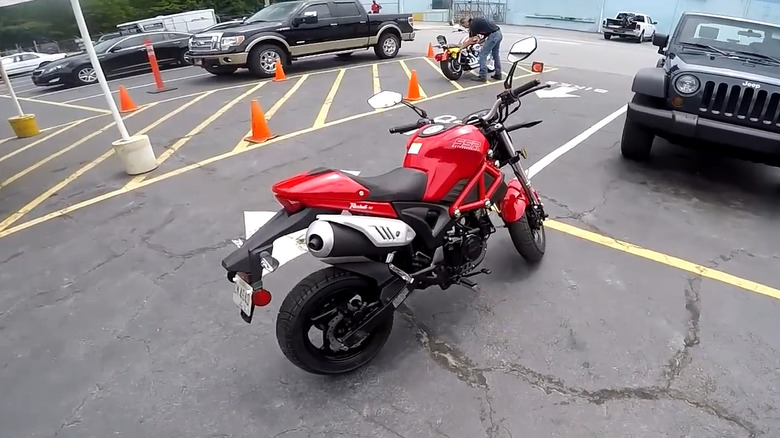 A red SSR Razkull 125 mini motorcycle parked on concrete in a lot next to a Jeep Wrangler in the background.