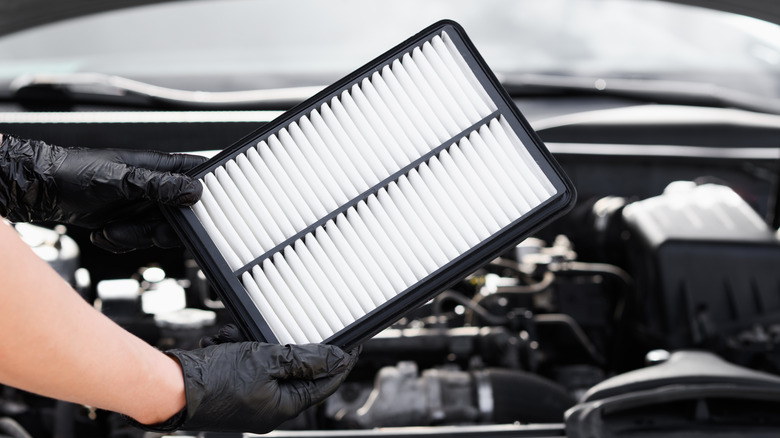 person holds air filter in front of car engine