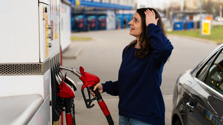 A woman holding a red gas nozzle looking shocked