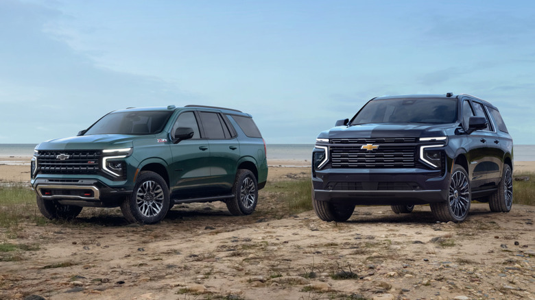 A navy blue Chevrolet Suburban and green Chevrolet Tahoe at the beach, front 3/4 view