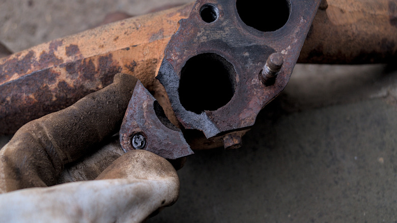 A rusty exhaust manifold from a car engine with a corner broken off