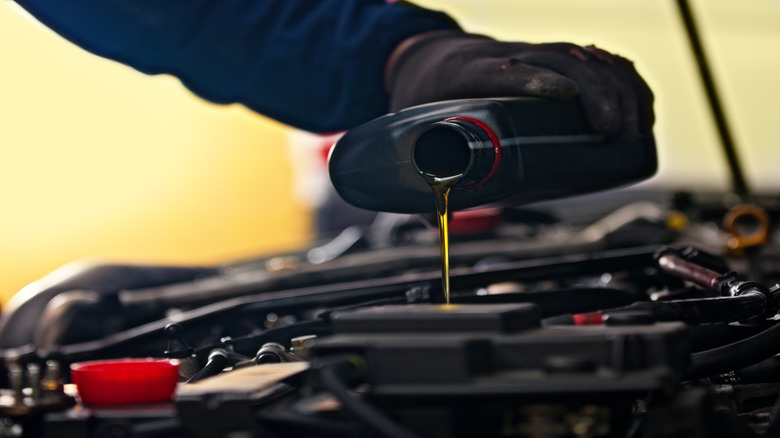 A person wearing black mechanic's gloves pouring oil into a car's engine