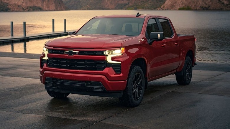 Radiant red tincoat Chevrolet Silverado 1500 Z71 parked on a wet pavement with a lake and mountains in the background