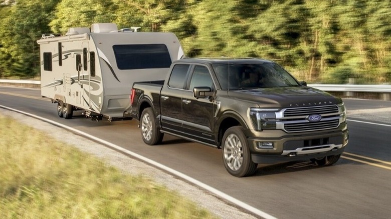 Ford F-150 Platinum Plus towing a travel trailer on a paved road with trees in the background