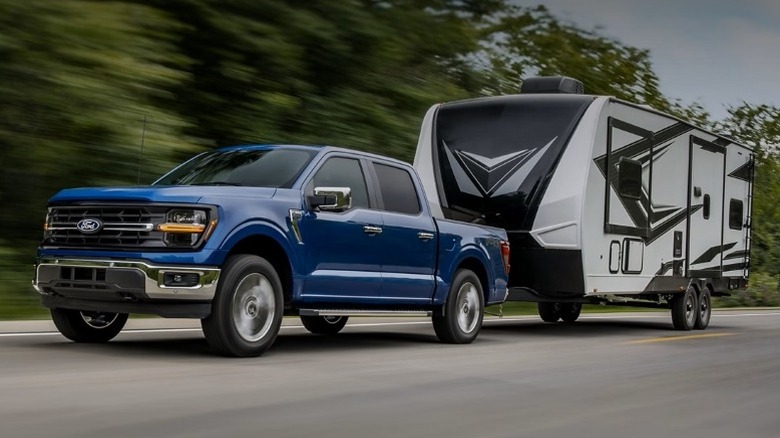Ford F-150 towing a travel trailer on a paved road with trees in the background