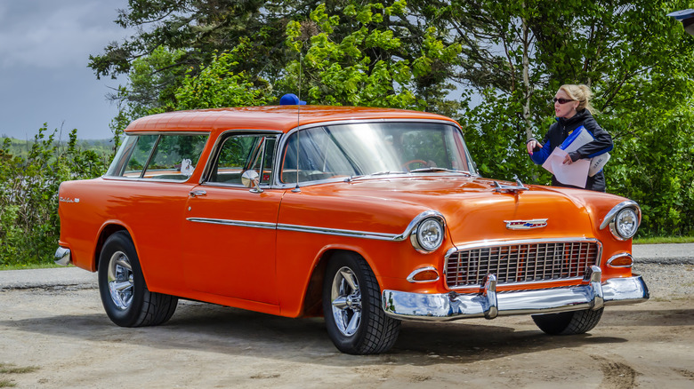 Red 1955 Chevy Nomad parked near trees on a cloudy day