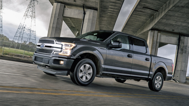 A 2018 Ford F-150 in gray driving past an underpass, front 3/4 view