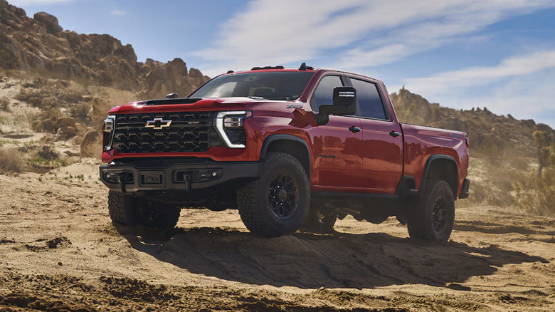Red Chevy Silverado 2500 HD pickup on dirt with mountains in background