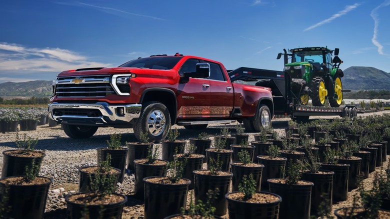 Red Chevrolet Silverado HD 3500 towing John Deere tractor past potted plants